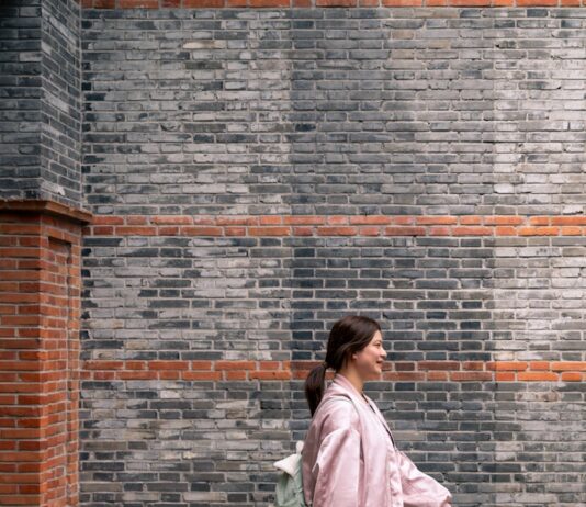 일상 속 걷기, 건강을 지키는 가장 손쉬운 비결 A woman walks along a brick wall.